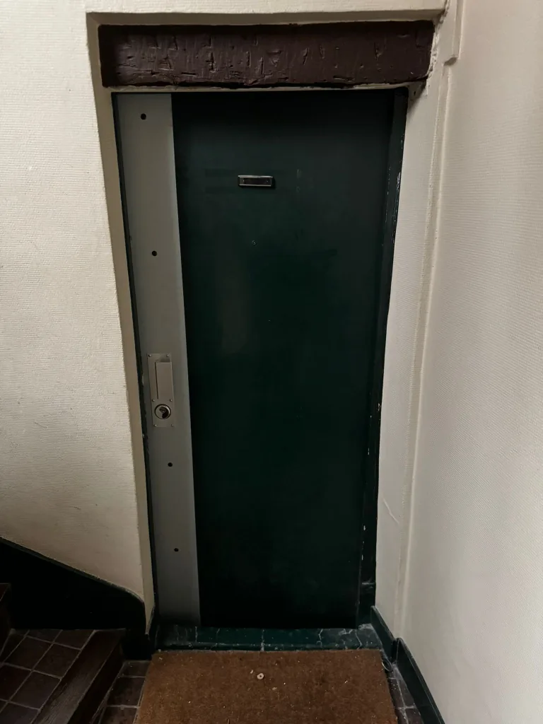 Plat de recouvrement métallique posé sur la tranche d'une porte verte, Villa de l'Astrolabe, Vaugirard, Paris 15e