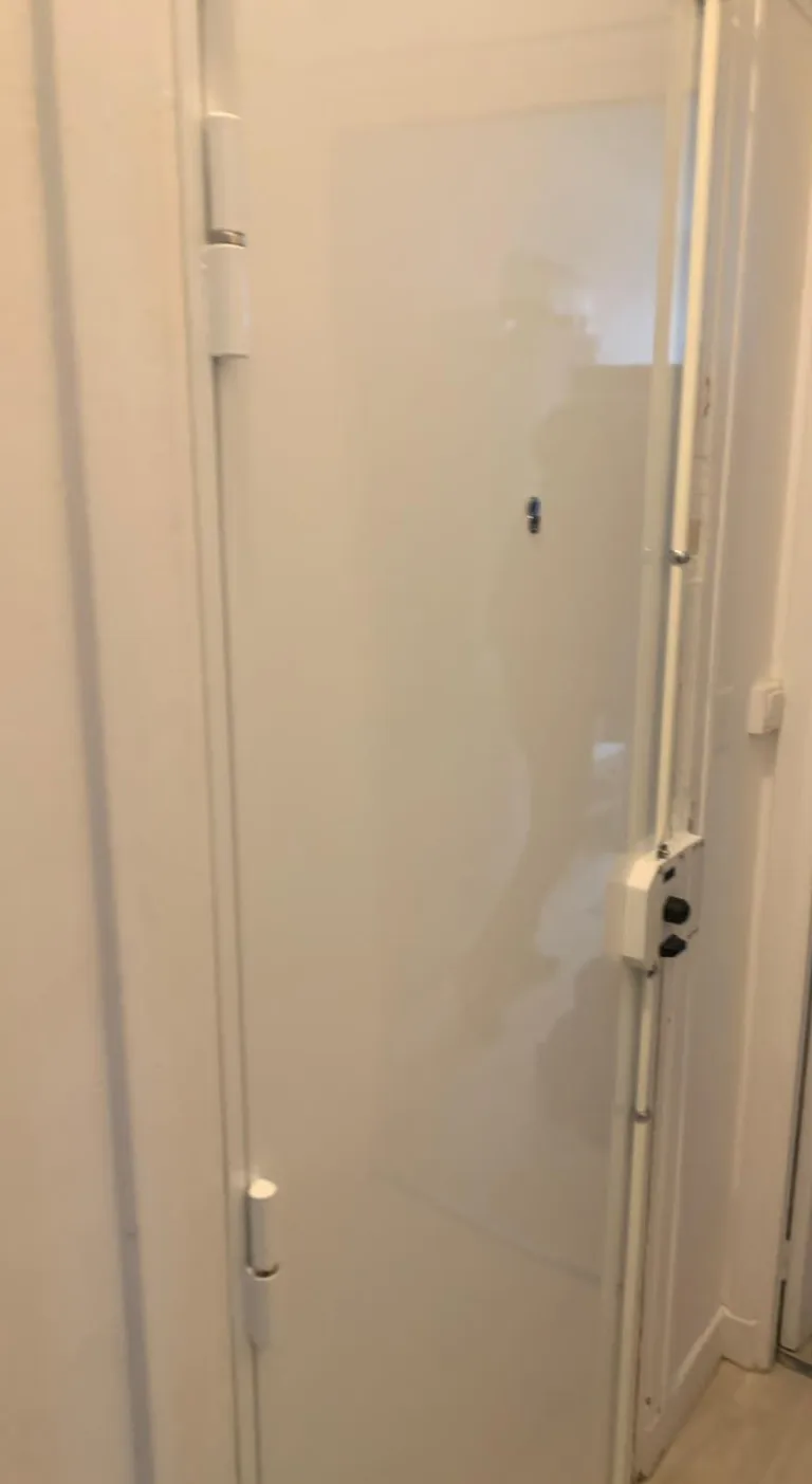Porte blindée blanche ouverte, rue Élisabeth Vigée Le Brun, Paris 15e : barre de pivot, paumelles renforcées et coffre de serrure visibles sur la tranche